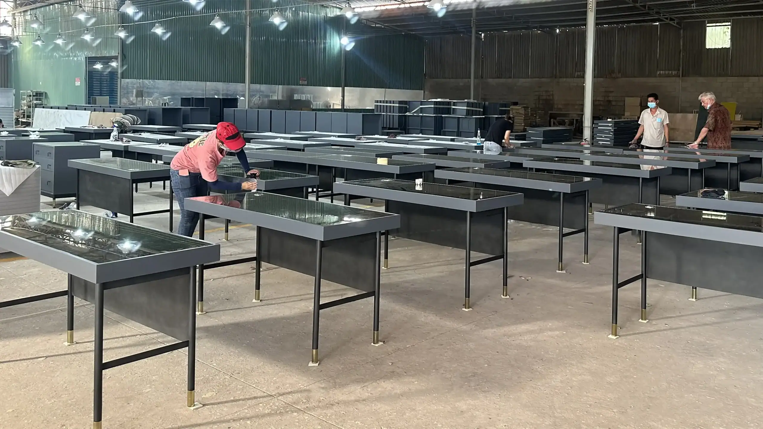 KNM furniture staff performing final inspection and quality checks on powder-coated metal desks with lacquered tops.
