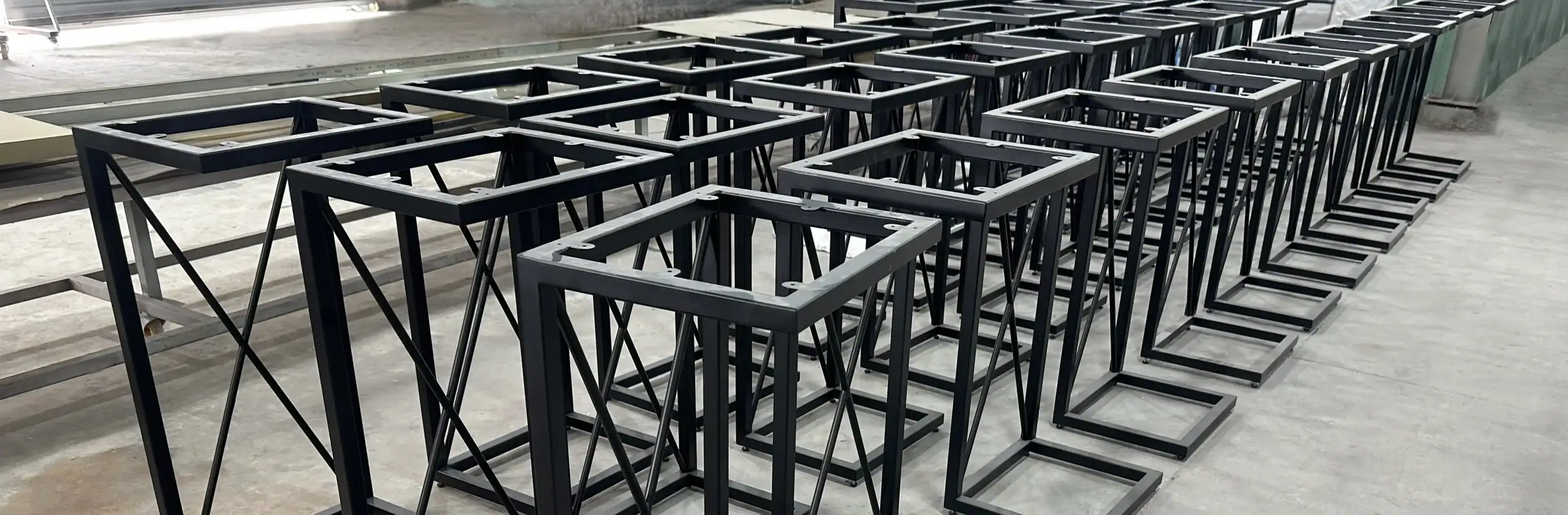 Geometric metal side table frames with black powder coat finish, ready for top installation in the manufacturing facility.