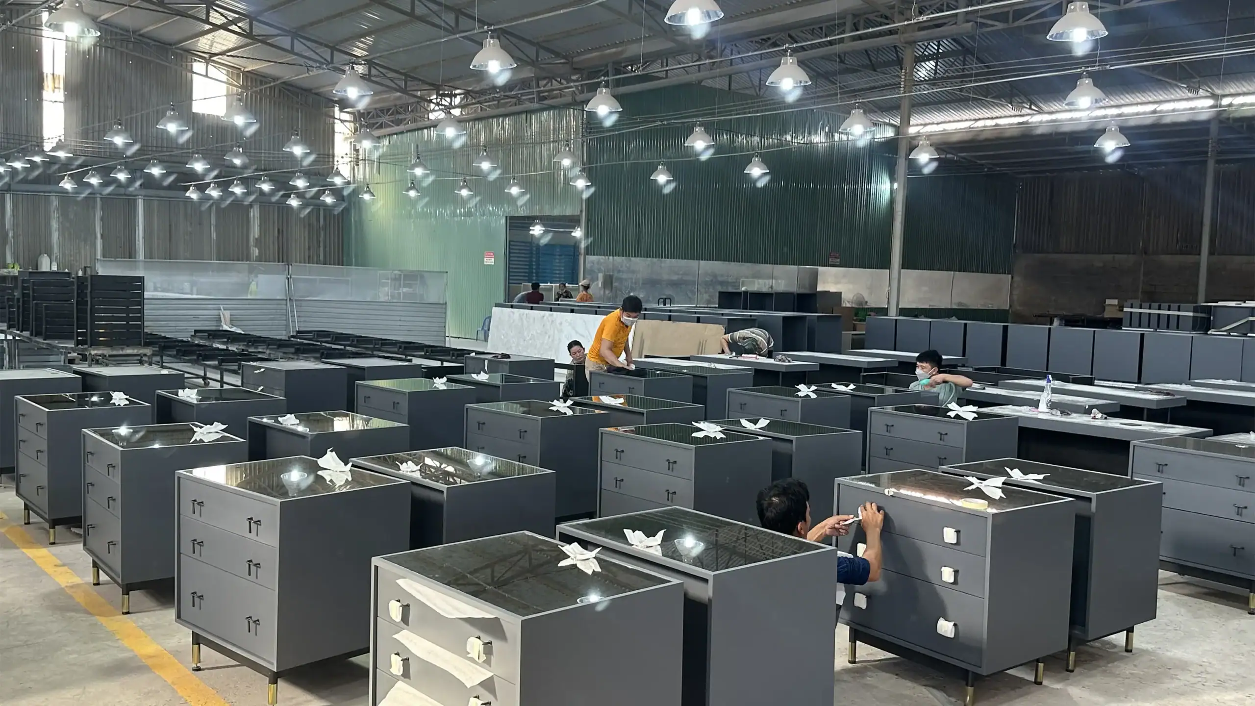 Mass production of storage cabinets with black powder-coated legs and glass/composite tops during final assembly.