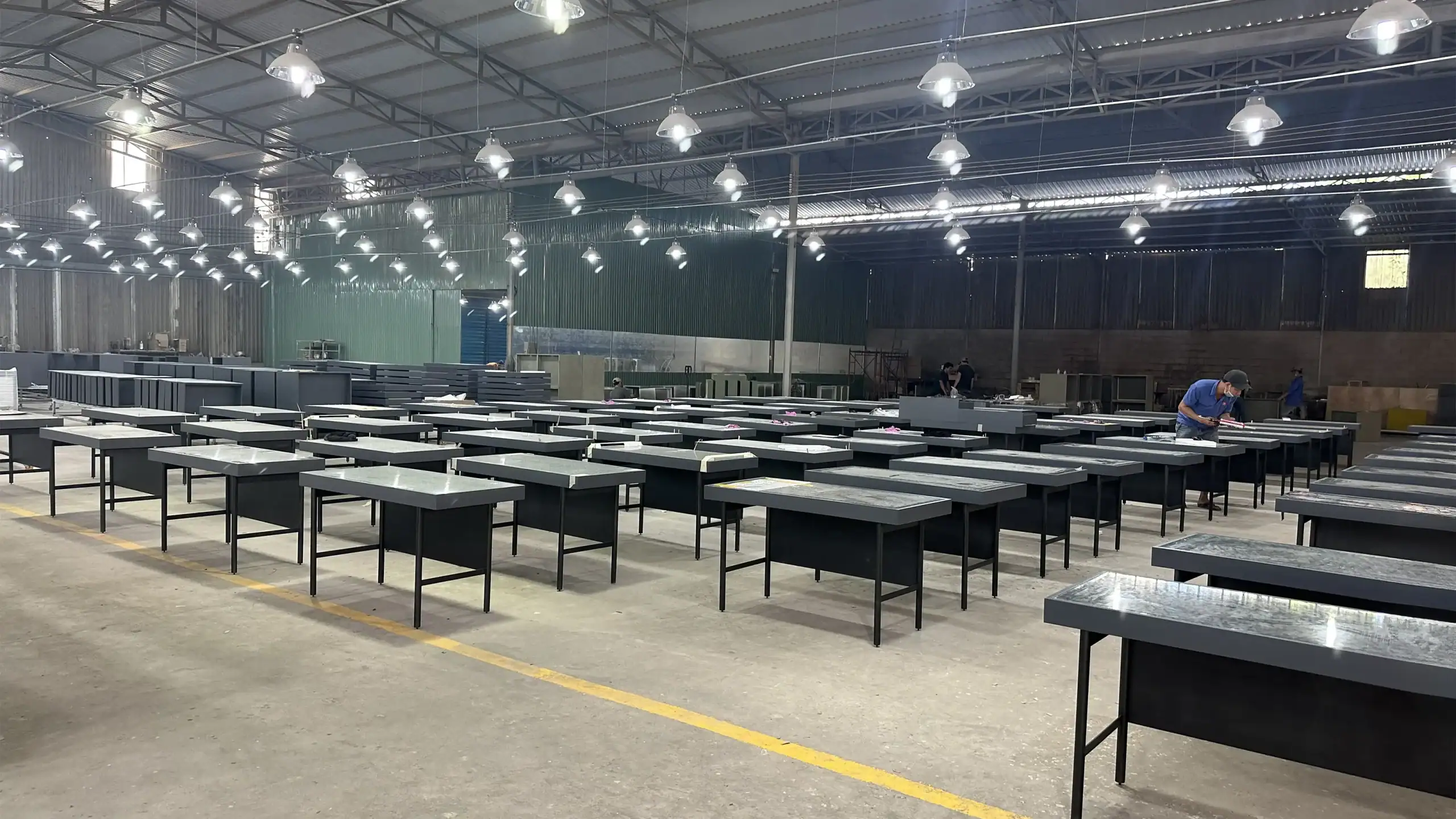 Batch of hospitality desks/cabinets with grey powder coated metal legs and black lacquer tops in the finishing area.