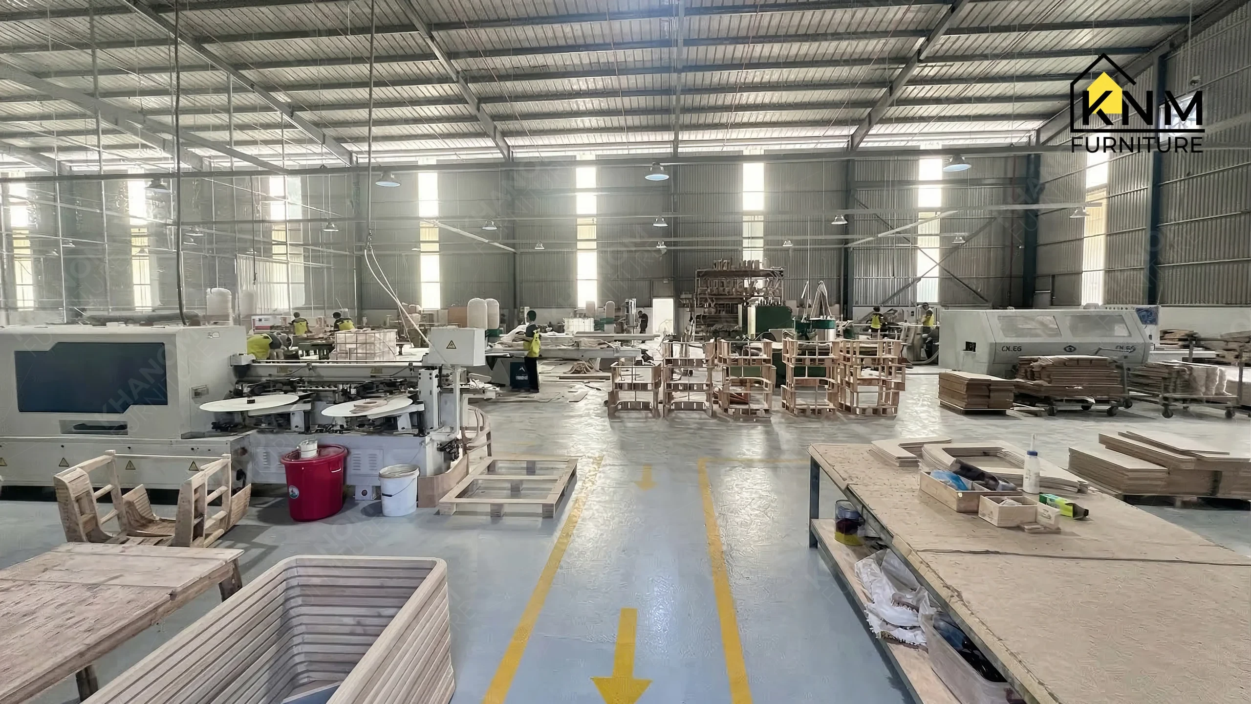 A wide angle view of heavy woodworking machinery and yellow safety lines on the floor at Khanom Furniture (KNM Furniture), a professional furniture factory Vietnam.