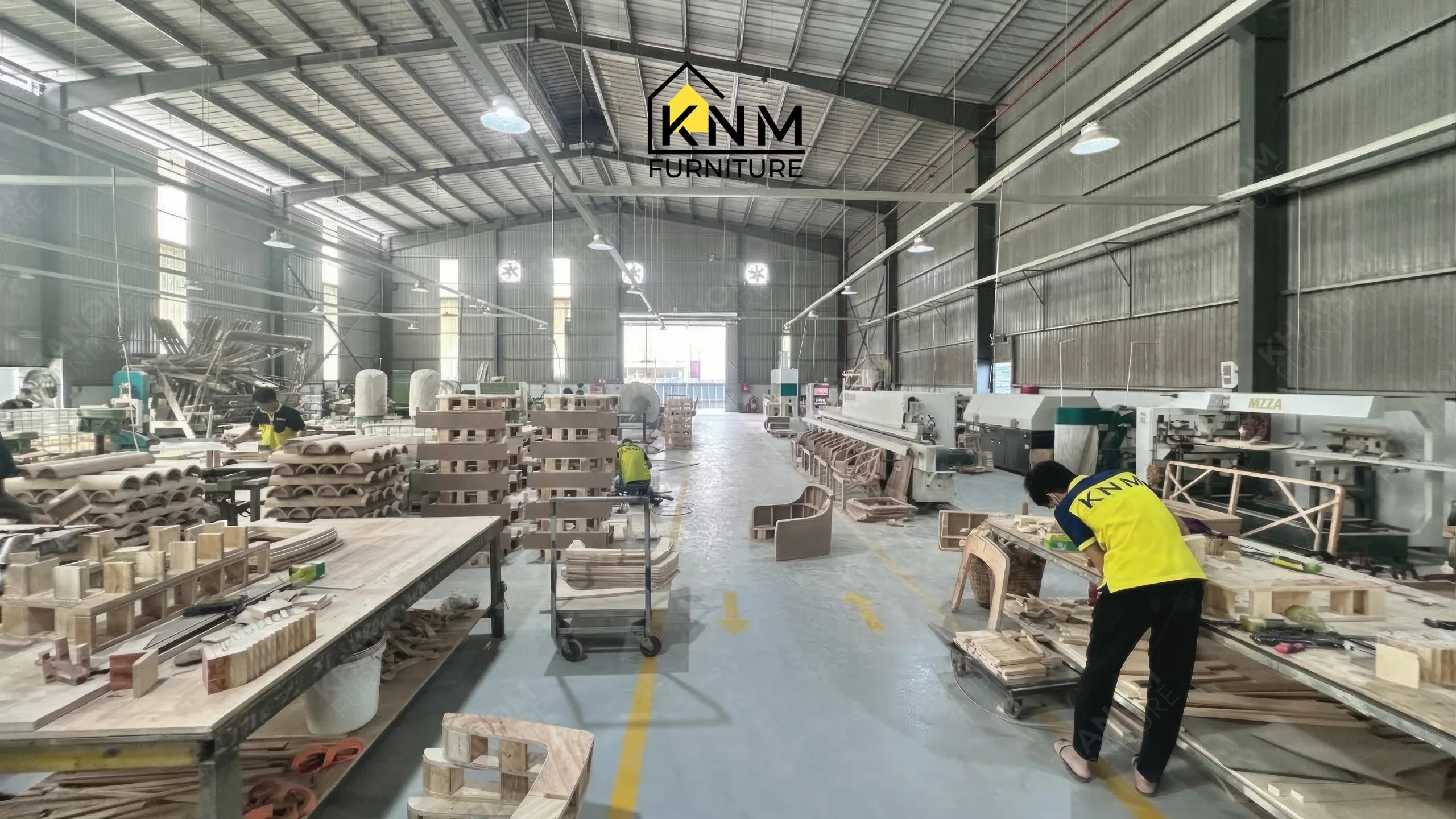 Large stacks of semi-finished curved wood components and workers assembling furniture at Khanom Furniture (KNM Furniture), a solid wood furniture factory Vietnam.