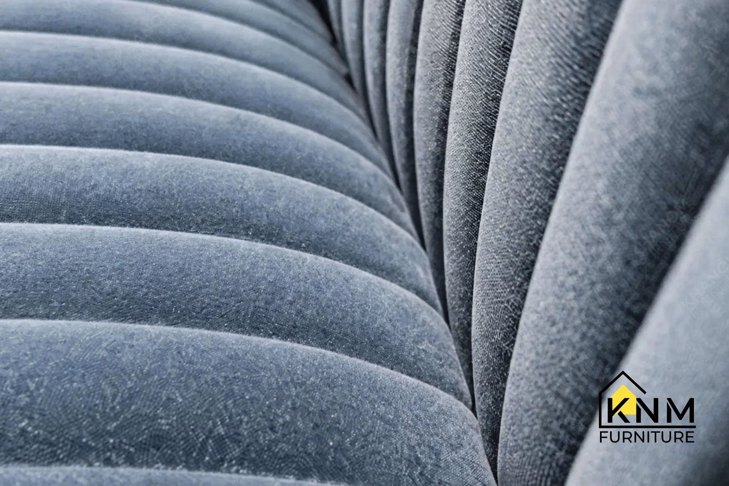 A detailed material zoom of the blue velvet channel tufted sectional by Khanom Furniture, showing the textile texture adjacent to the walnut veneer structure.