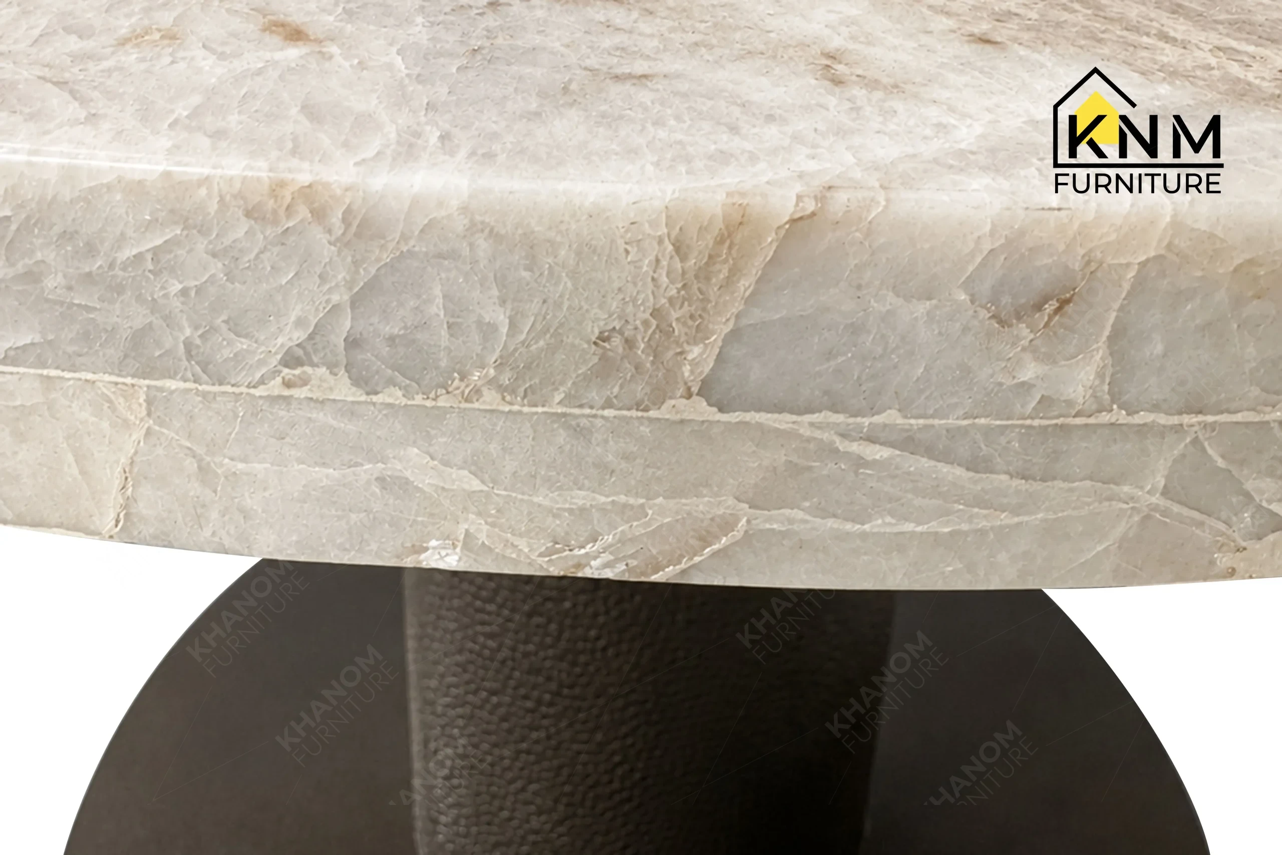 A detailed material zoom of the round stone top metal dining table by Khanom Furniture, showing the gloss Tuffskin finish on the local Taj Mahal stone.