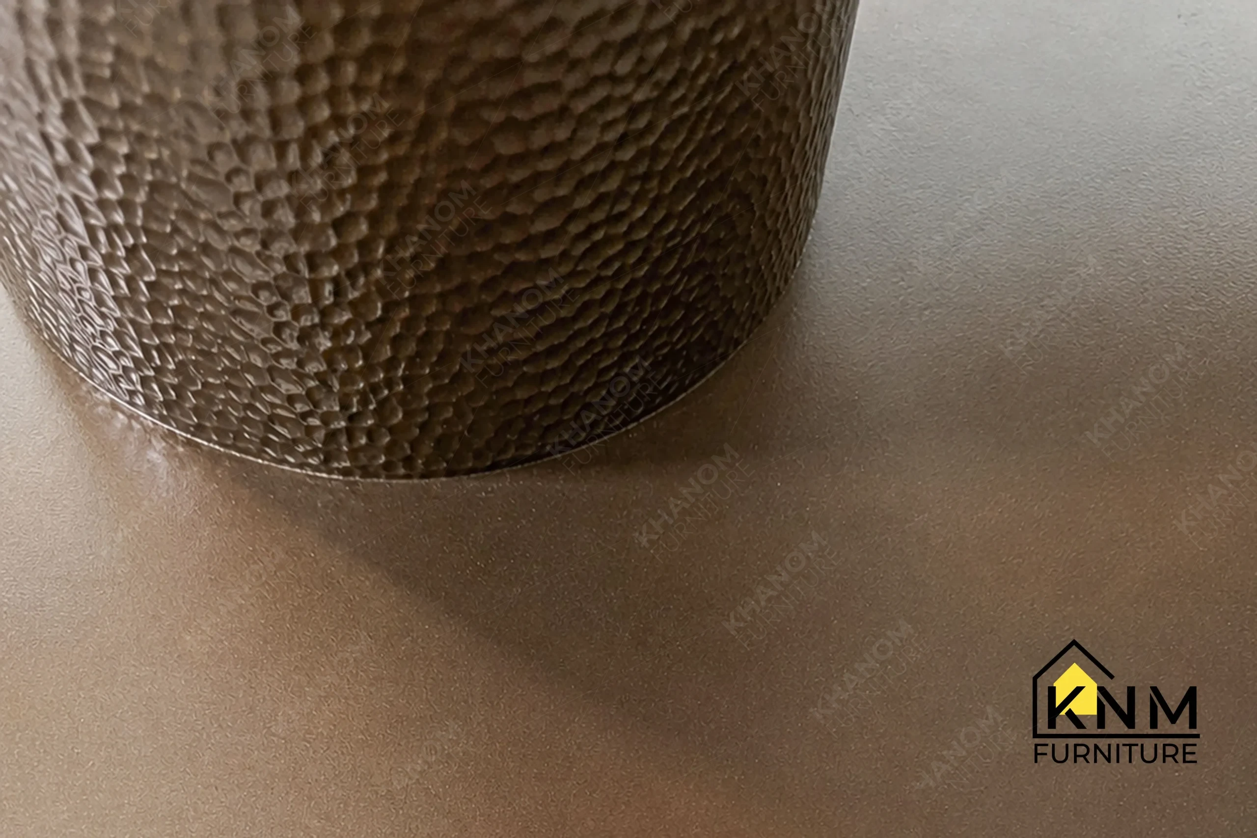 A technical detail of the round stone top metal dining table from Khanom Furniture, describing the Hammered Bronze texture and Antique Brass base.