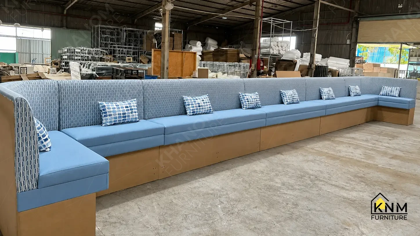 Extended blue upholstered banquette seating with patterned welt-trimmed pillows manufactured for a hospitality F&B project by Khanom Furniture (KNM Furniture) Vietnam