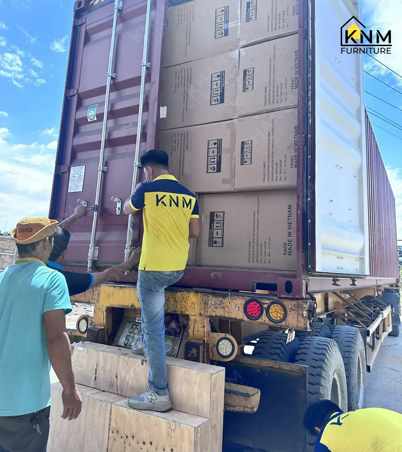 Khanom Furniture (KNM Furniture) logistics team loading labeled project cartons into a shipping container for ocean freight export to the United States, KNM logo visible upper left.