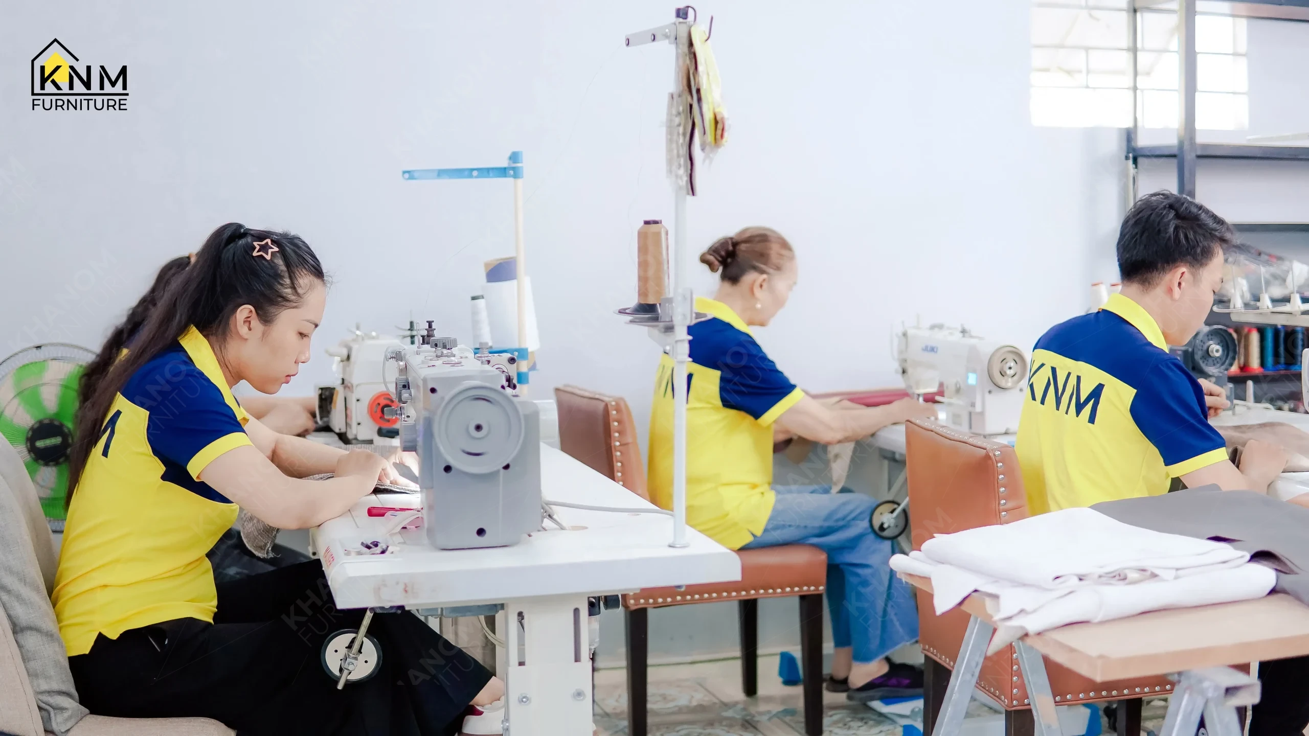 Row of Khanom Furniture (KNM Furniture) upholstery staff at flatbed and overlock sewing stations constructing seating fabric panels in the factory sewing room, Vietnam