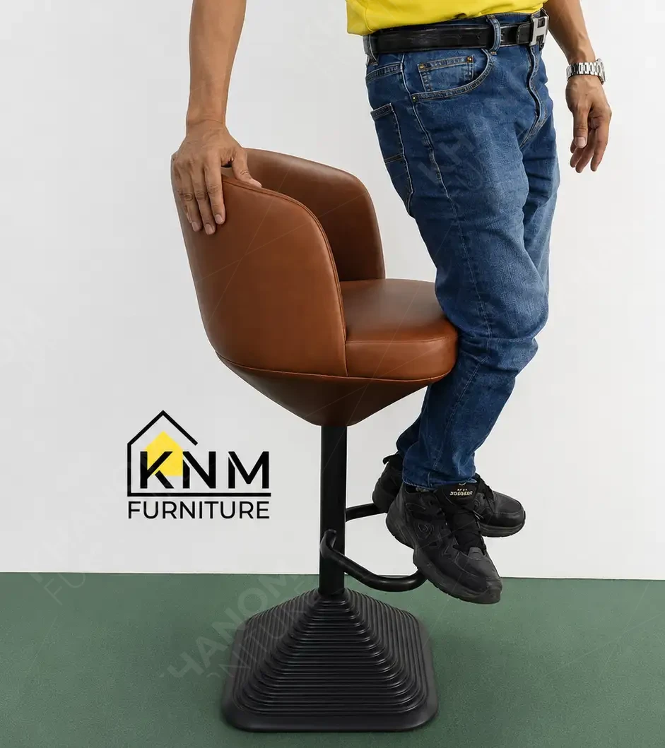 Khanom Furniture QC technician performing a physical stability and off-axis load test on a brown leather upholstered barstool with metal pedestal base, simulating dynamic commercial use conditions.
