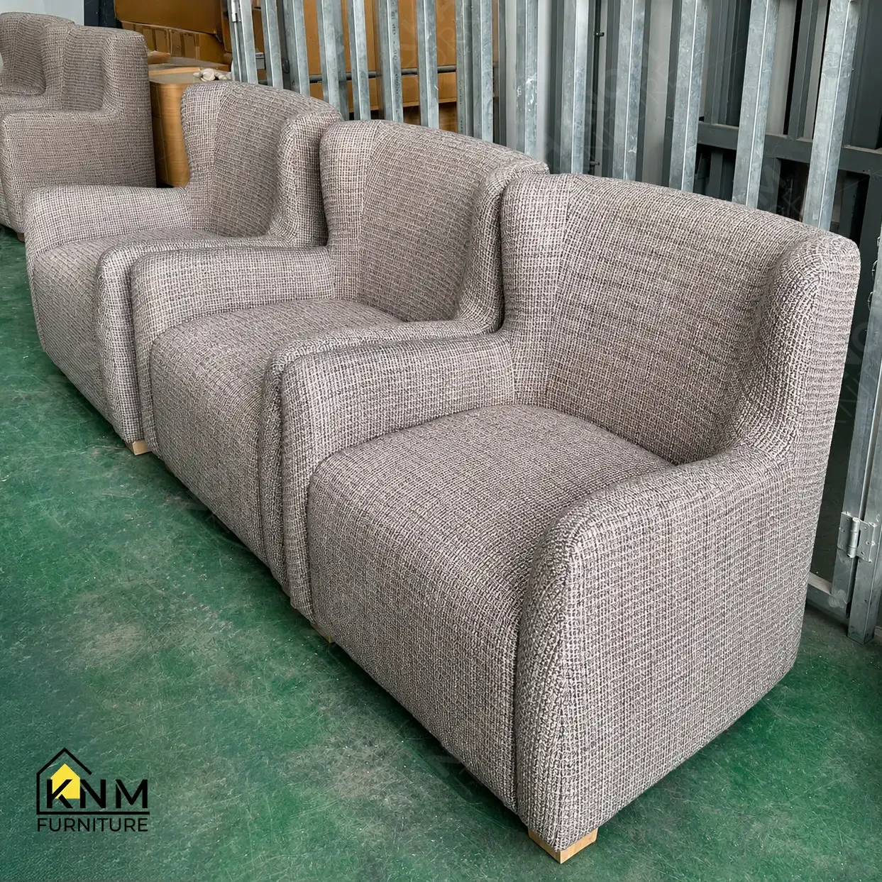 Row of finished grey tweed upholstered curved armchairs staged on the factory floor for quality inspection before export packaging, Khanom Furniture (KNM Furniture) Vietnam